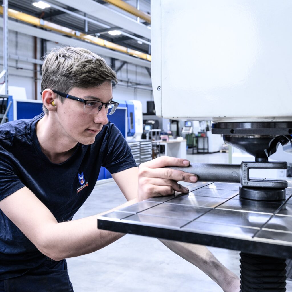 Person arbeitet in einer Produktionshalle an einer Mess- oder Prüfvorrichtung auf einem Maschinentisch.